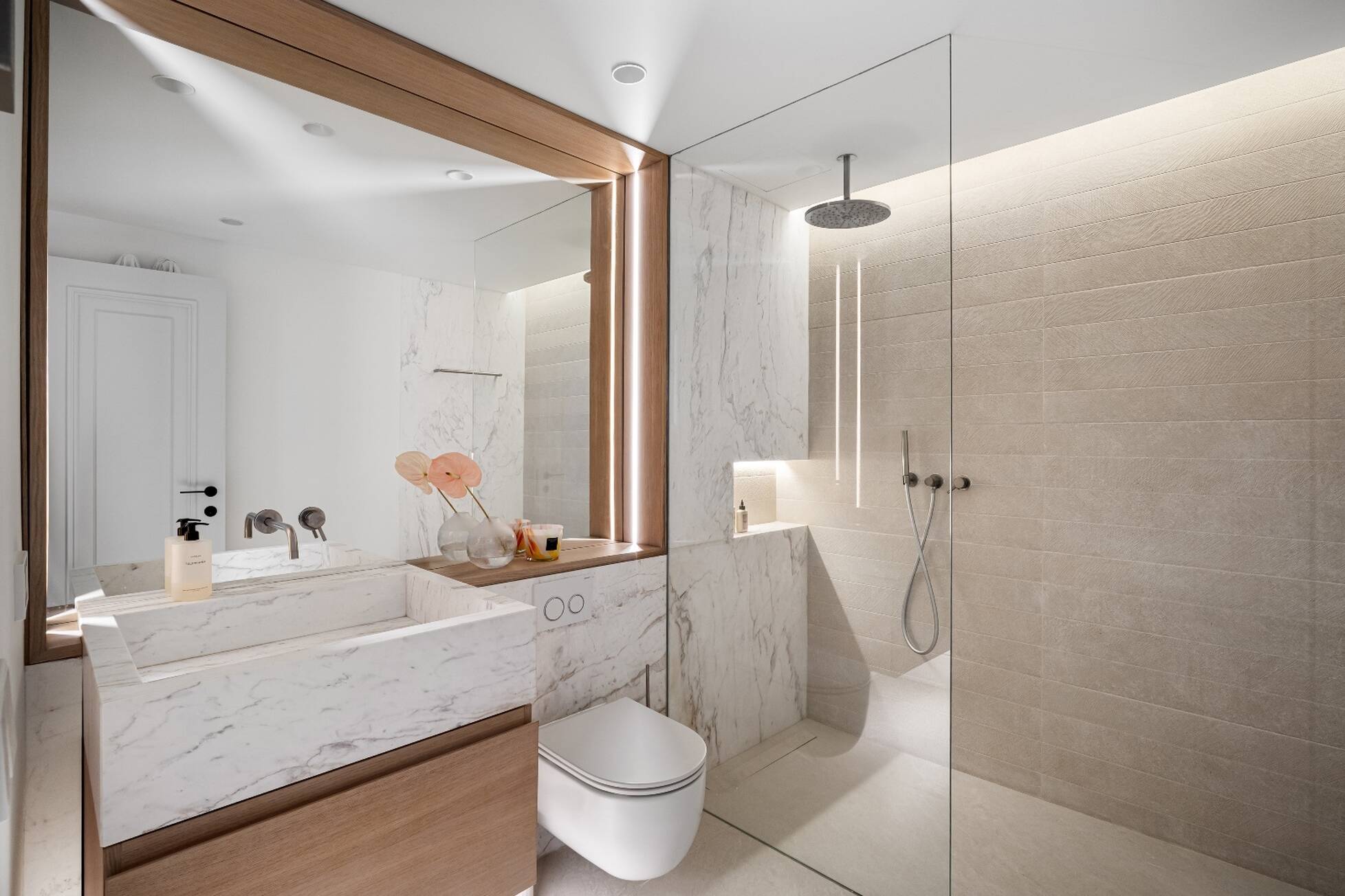 Bathroom clad in book-matched marble with a walk-in rain shower behind glass