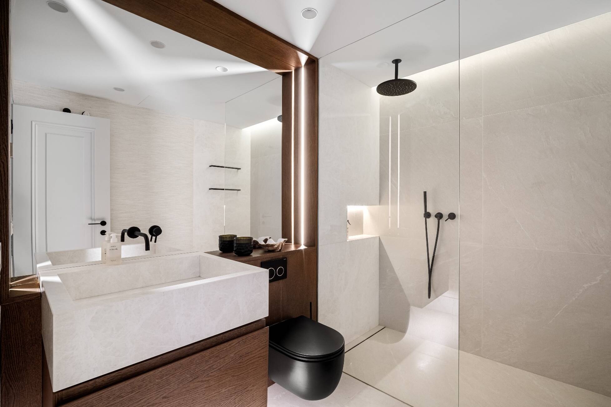 Guest bathroom in cream stone with black fittings and a backlit oak mirror