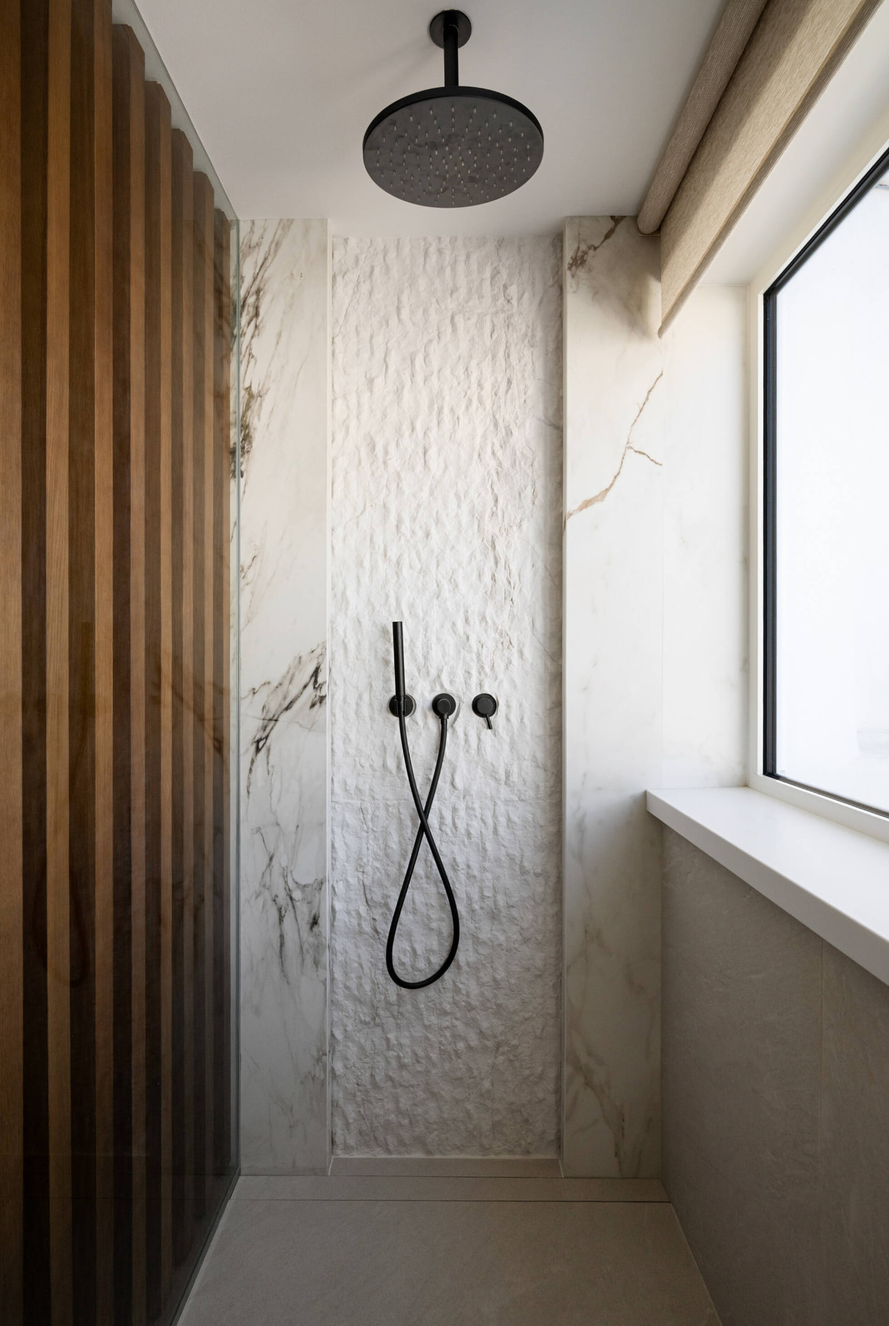 Walk-in rain shower clad in marble with a textured stone feature panel
