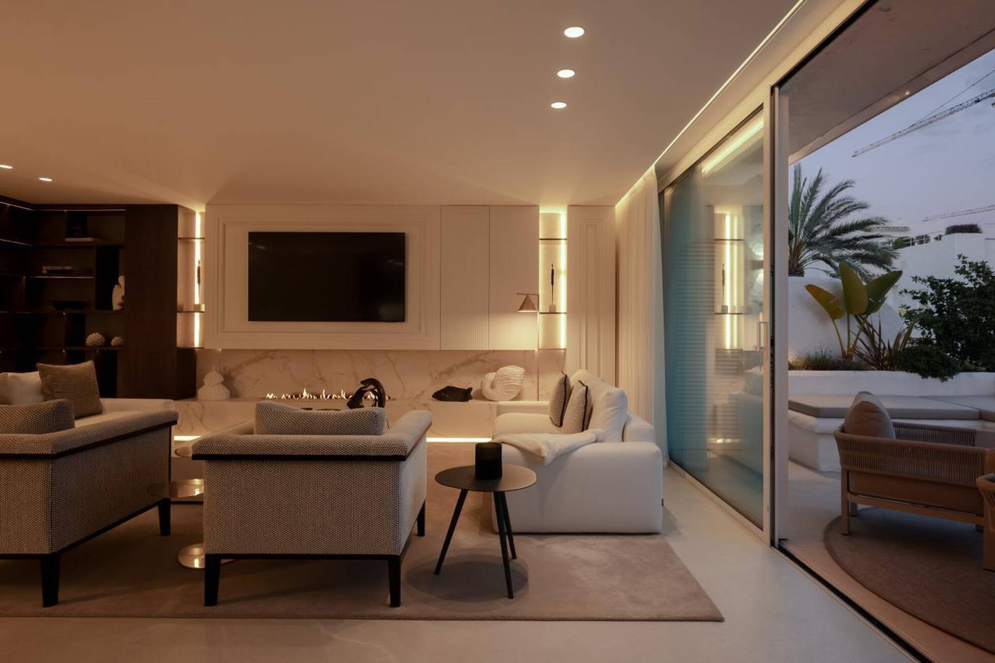 Evening view of the lounge with lit fireplace and open sliding doors to the garden terrace