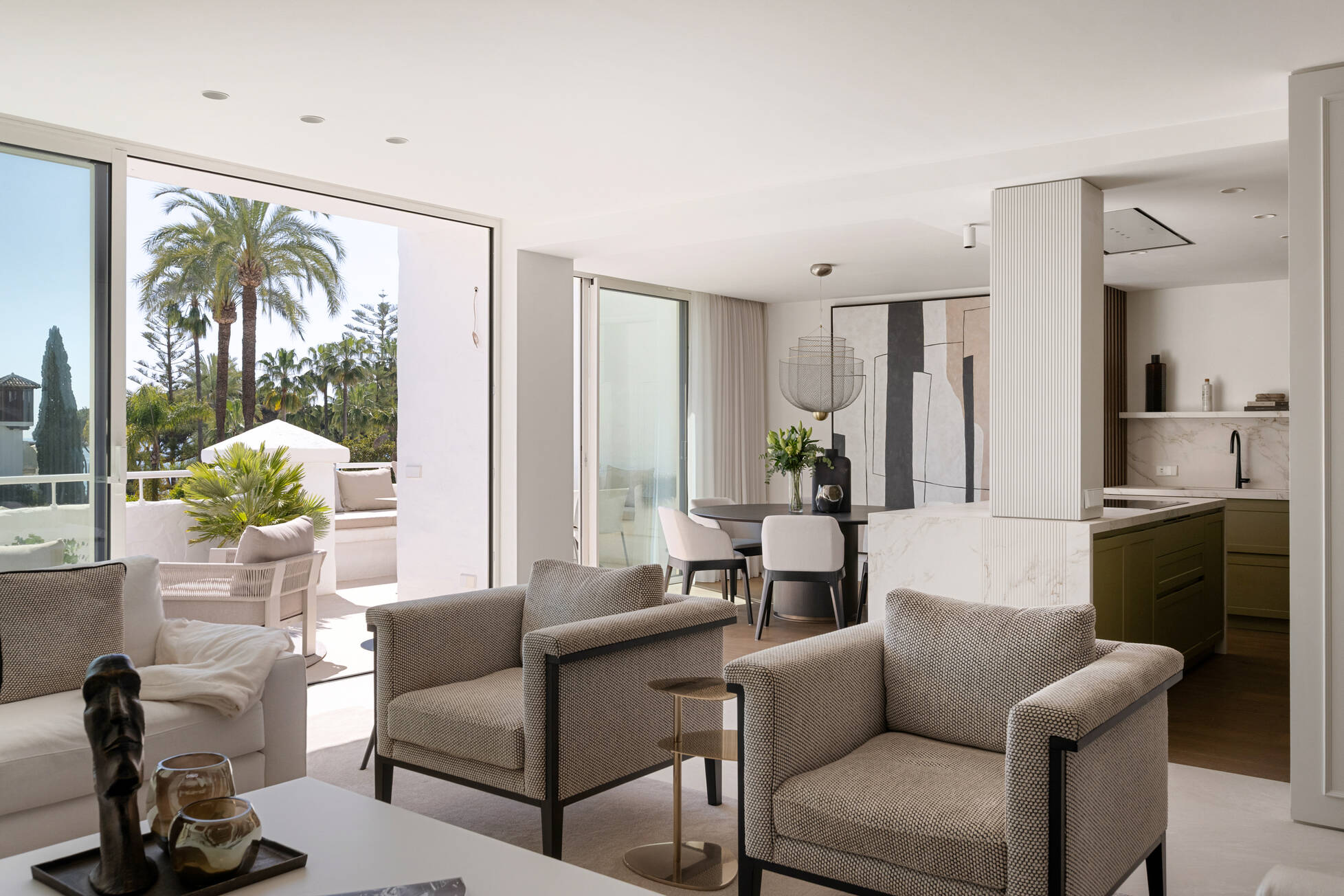 Open-plan living room of the Alhambra del Mar penthouse with sliding doors opening onto a palm-shaded terrace